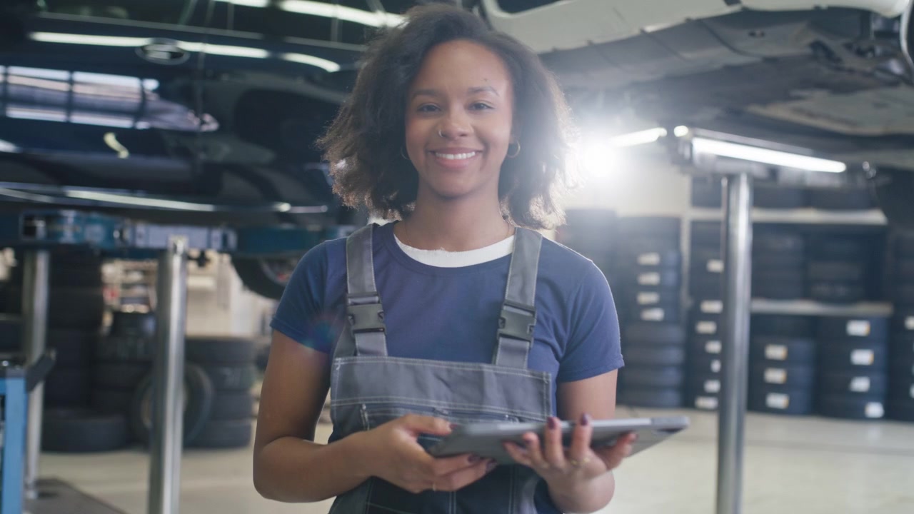 Ritratto di donna afroamericana sorridente, meccanico d'auto, che usa un tablet in un servizio di manutenzione.
