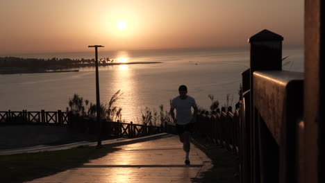 silhouette of man running uphill with sunset above sea in background, slow motion