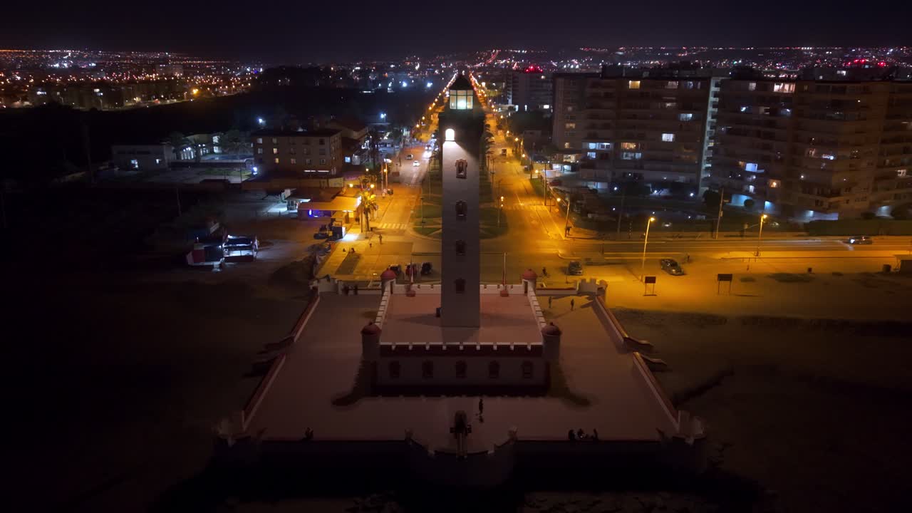 Aerial view around the illuminated Faro Monumental lighthouse, evening in Chile