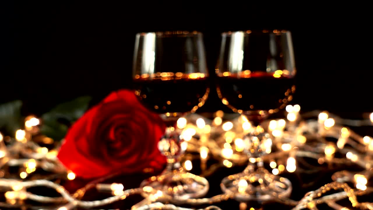 Copa de vino y una rosa sobre un fondo de guirnaldas luminosas. Fuera de foco.