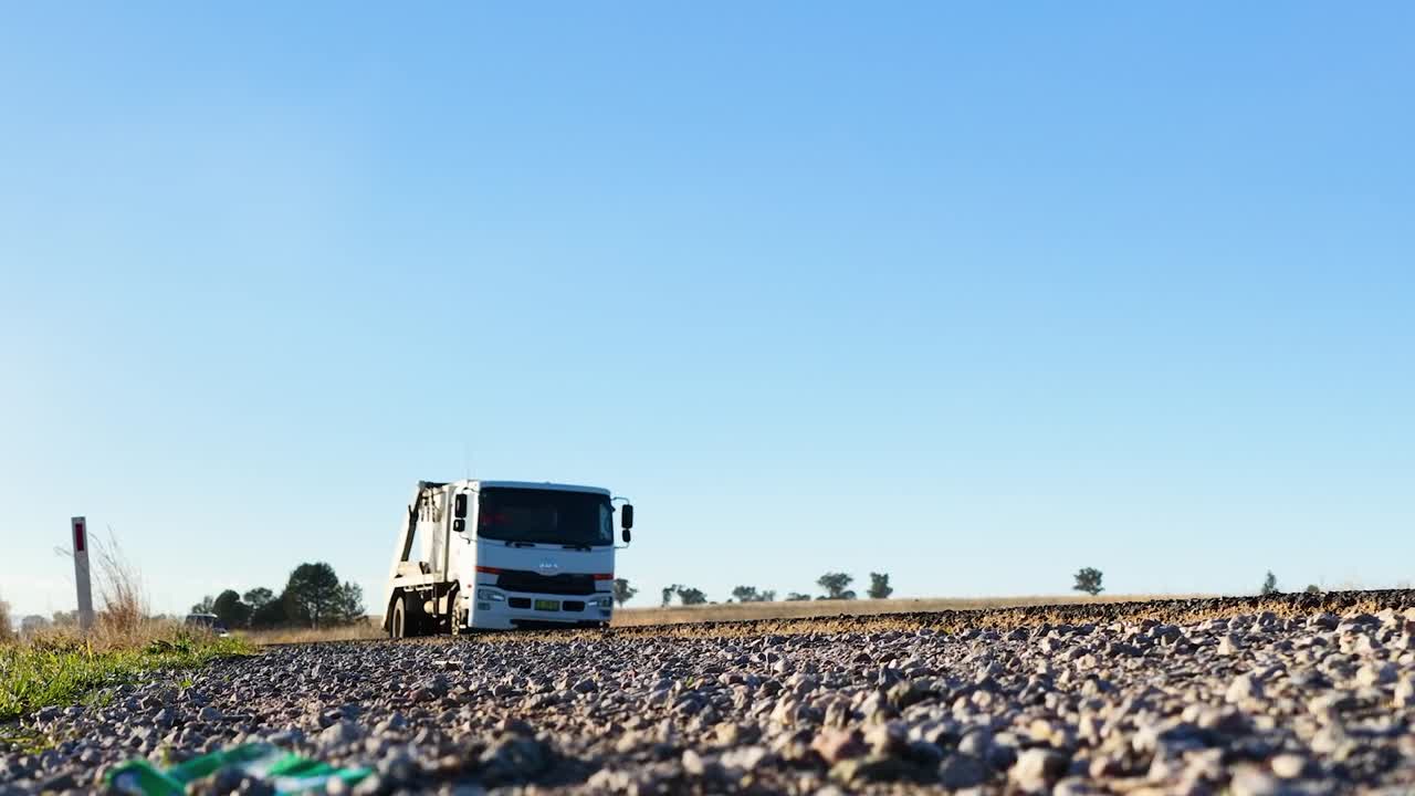 Camion commerciali e un'autovettura percorrono una strada sterrata polverosa in pieno giorno