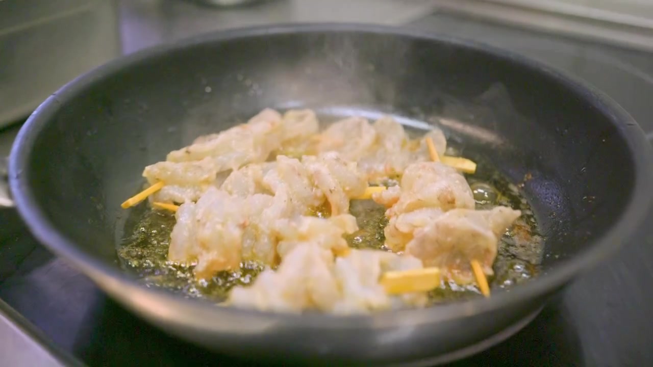 Slow motion close up push in shot of prawns frying in hot oil in a black pan on a kitchen stove with steam bubbling oil and gentle sizzling
