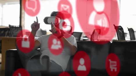 Animation-of-digital-icons-and-data-processing-over-caucasian-man-wearing-vr-headset-at-office