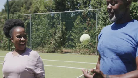 happy senior african american couple playing tennis and high fiving at tennis court in slow motion