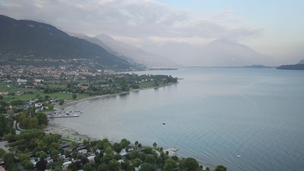 A stunning drone shot of the Italian lake town Dongo in Lake Como, flying over the town with majestic mountains and the shimmering lake creating a breathtaking backdrop.
