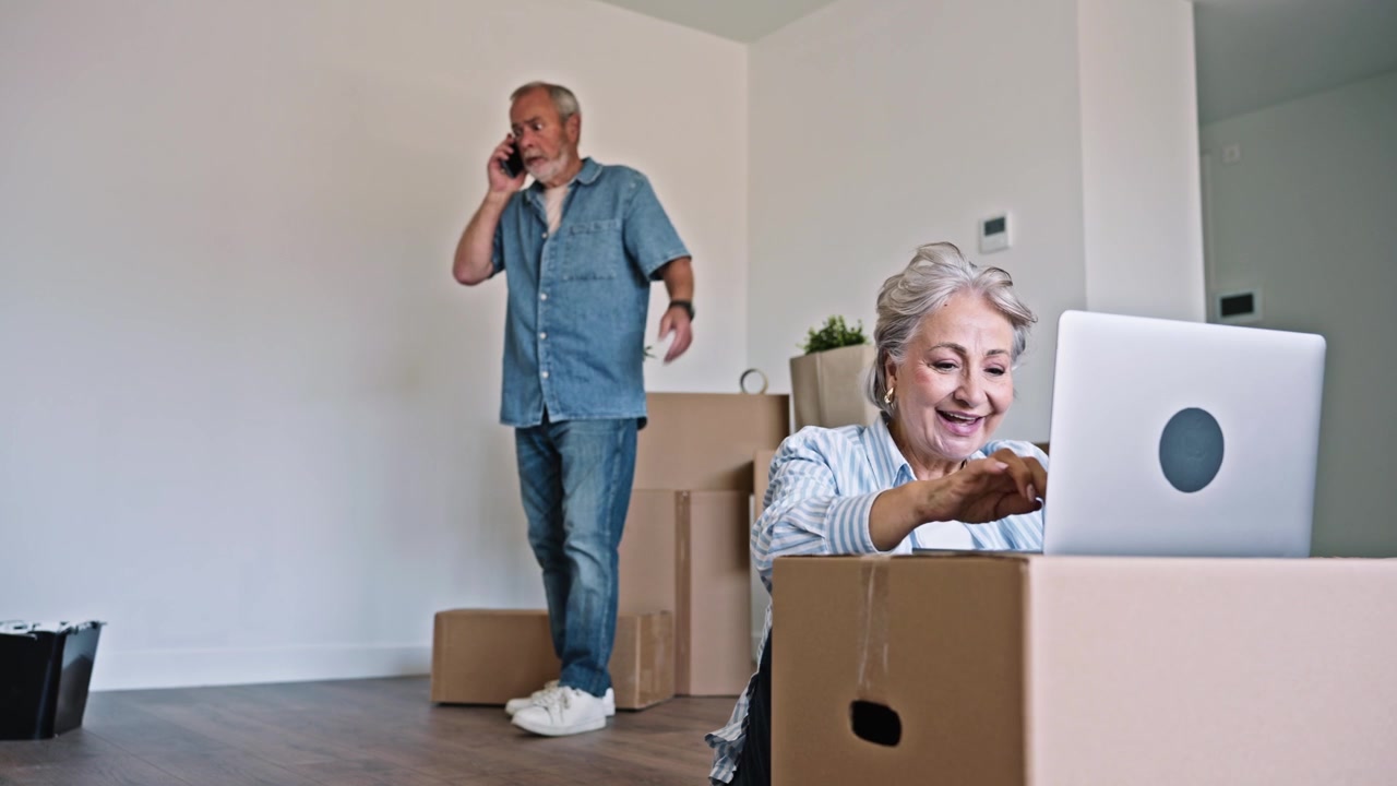 Senior Couple Using Laptop and Phone While Moving into New Home