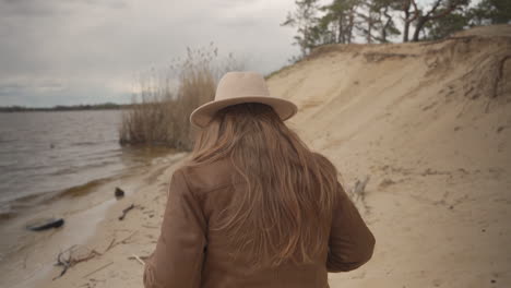 una mujer pelirroja irreconocible caminando a orillas del lago