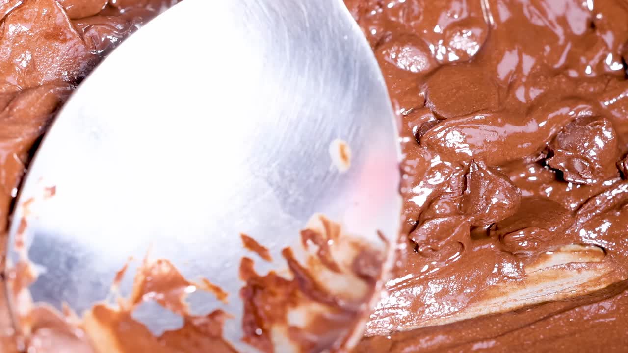 A spoon gently stirs smooth, melted chocolate, showcasing its glossy texture and rich color.