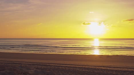 A-striking-golden-yellow,-fiery-orange-sunset-across-a-deserted-beach-scene