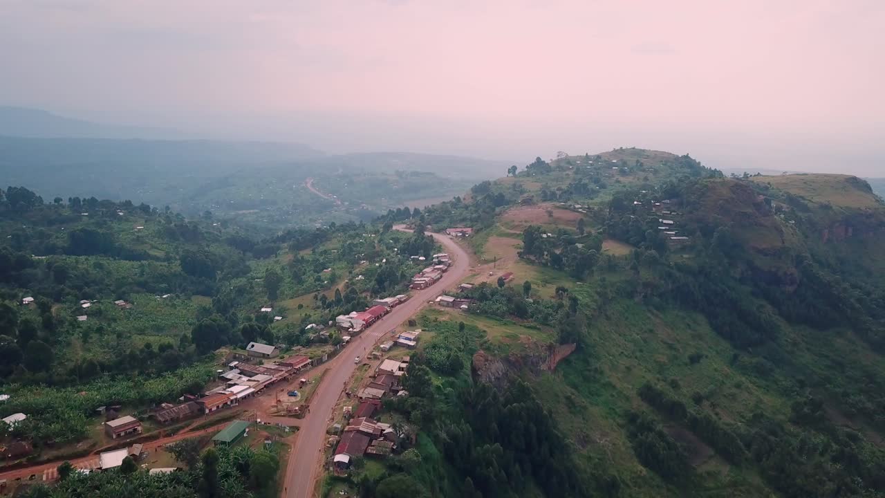 Aerial view of a trading center along a winding road nestled in the lush green mountain slopes of Mount Elgon National Park in Uganda with scattered buildings and dramatic elevation