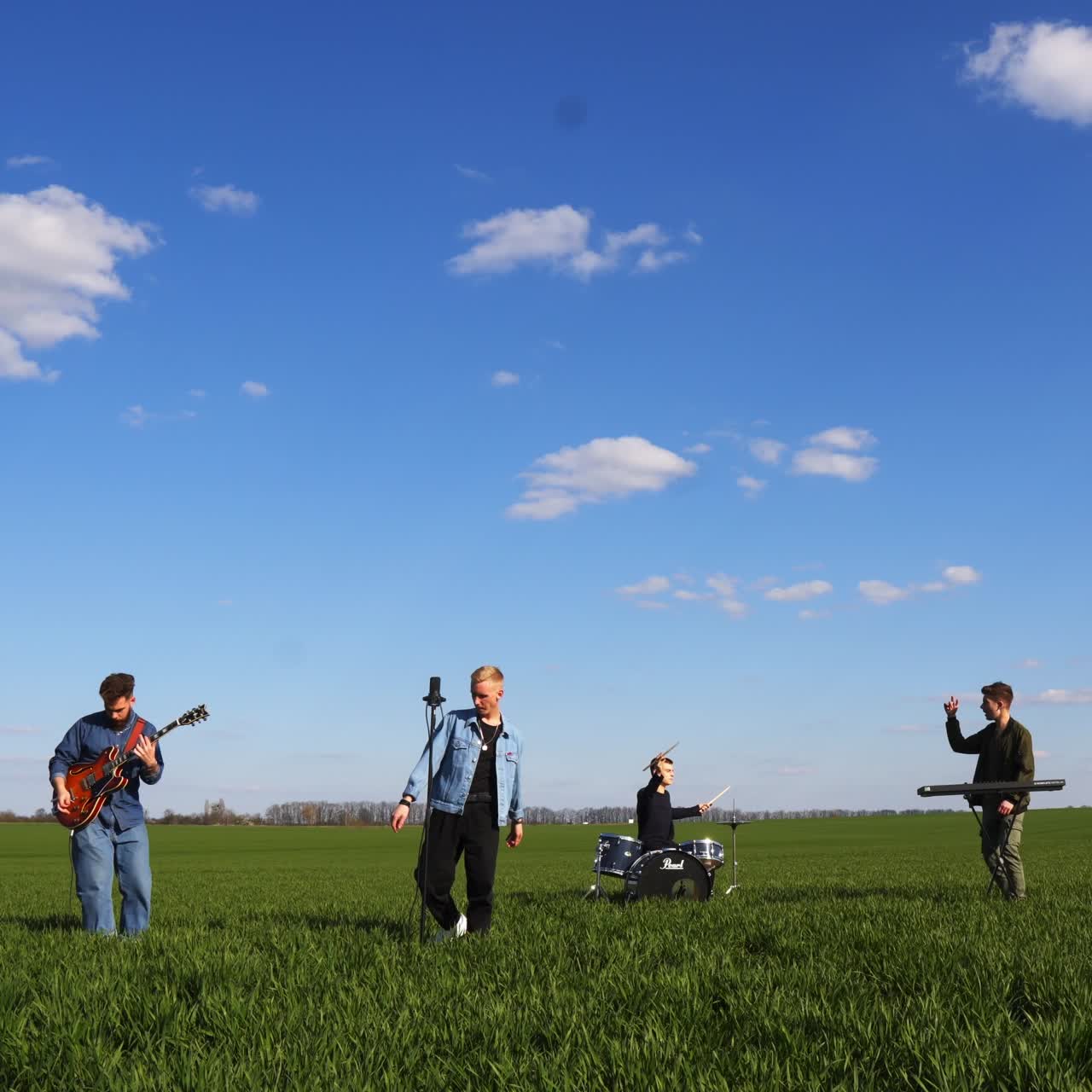 Boys band playing musical instruments and singing song. Music group of four young men performing music in the field in summer