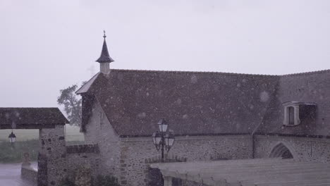 heavy rain pours over a rustic stone building, creating an intense and atmospheric scene