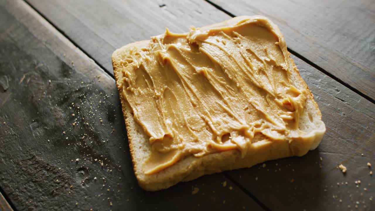 Video of close up of toast with peanut butter on wooden background