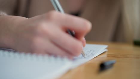 close-up of lady hand writing with pen, showing focus on notebook, pen cover lies on the table beside, capturing a quiet study scene