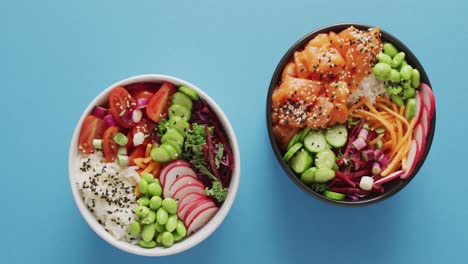 composition of bowls with rice, salmon and vegetables on blue background