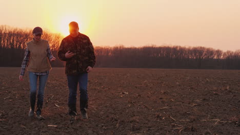 Two-Farmers-A-Man-And-A-Woman-Walking-Along-A-Plowed-Field-Talking