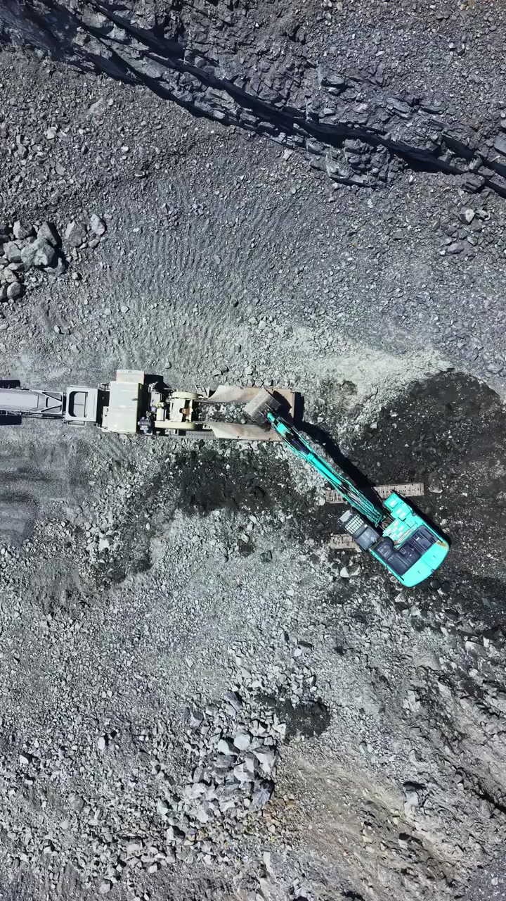 Excavator working at granite quarry digging and transporting stone material in daytime view from above