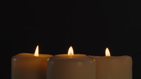 three lit candles on black background