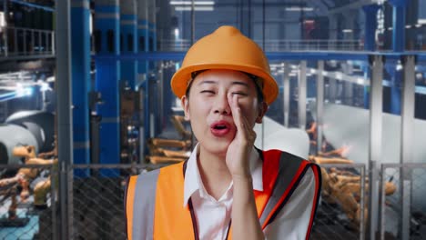 close up of asian female engineer with safety helmet yelling with hand over mouth while standing in factory manufacture of wind turbines