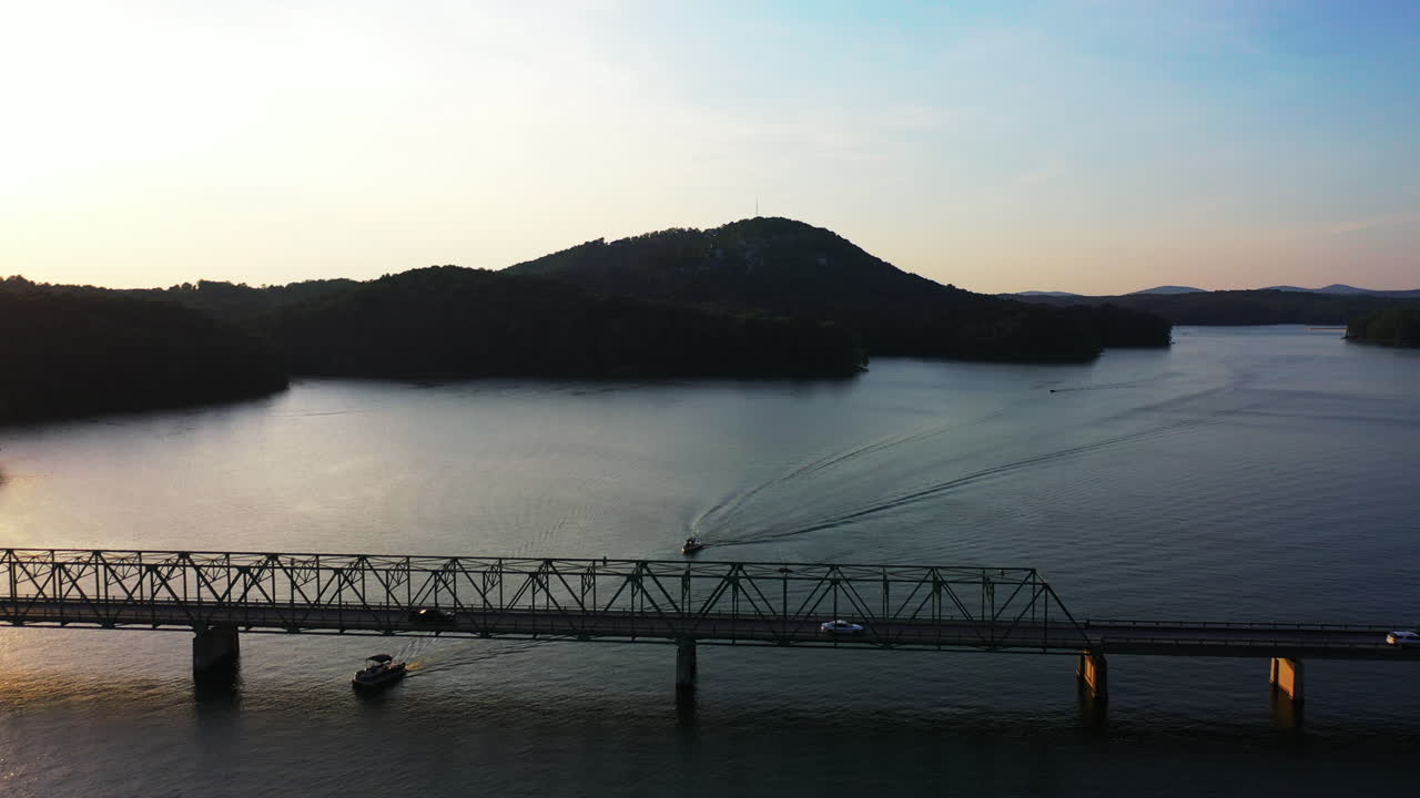 해가 지는 도로 다리 아래를 지나가는 배의 놀라운 항공 영상