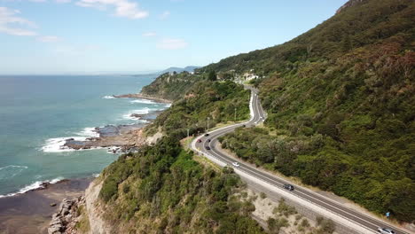 Antenne:-Drohne-Fliegt-über-Fahrzeuge,-Die-Entlang-Einer-Autobahn-Neben-Einer-Wunderschönen-Meeresküste-In-New-South-Wales,-Australien,-Fahren