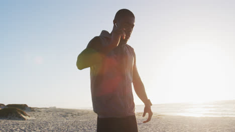 Hombre-Afroamericano-Revisando-El-Reloj-Inteligente,-Haciendo-Ejercicio-Al-Aire-Libre-Junto-Al-Mar