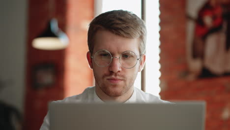 adult man is reading news in internet by laptop sitting in cafe in daytime portrait of pensive concentrated man with glasses