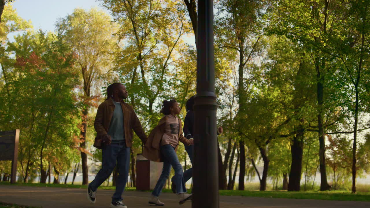 Familia afroamericana caminando juntos por el parque de otoño. Niño feliz tomado de la mano de sus padres.