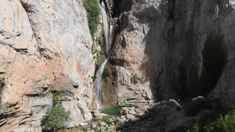 ascending shot at remorse waterfall in the mountains, as water falls from heights, carving a pond in stone as forming the environment