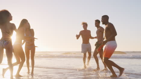 group of friends run through waves together on beach vacation