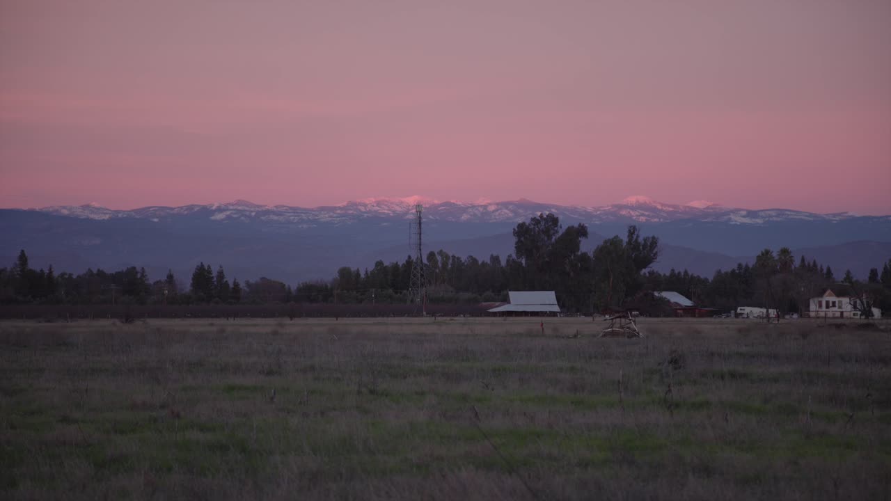 un cielo pastel sobre las montañas de sierra nevada con líneas eléctricas y un cobertizo en primer plano en clovis, ca, ee.uu.