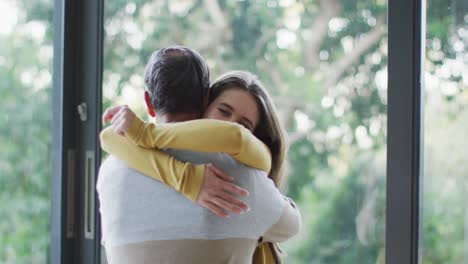 Happy-senior-caucasian-father-and-teenage-daughter-hugging-by-window-with-garden-view