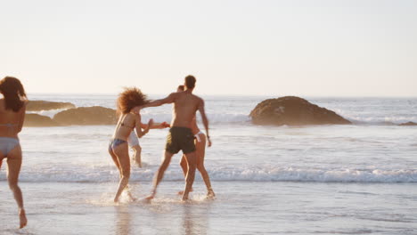 un grupo de amigos corren a través de las olas juntos en vacaciones en la playa