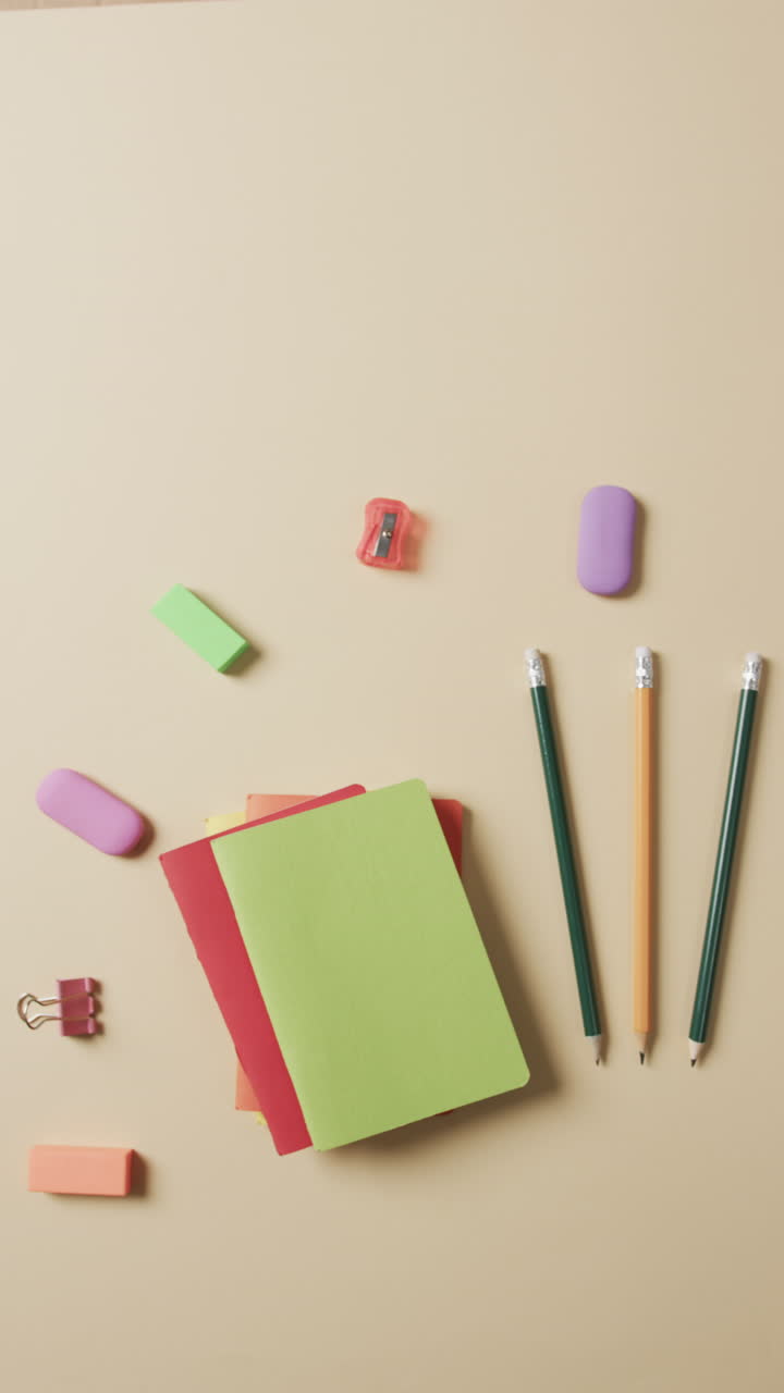 Vertical video of overhead view of school stationery on beige background, in slow motion