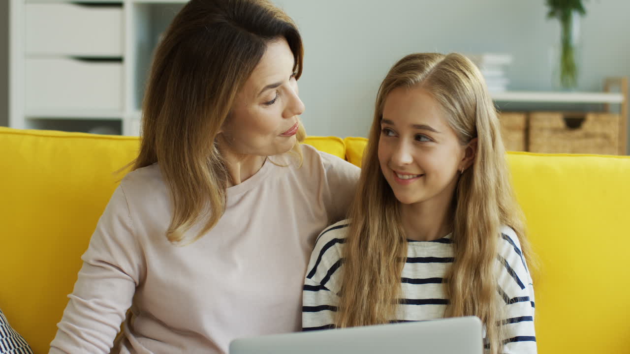 Blonde Mother And Daughter Making A Video Call With A Tablet While Sitting On Sofa In Living Room 1