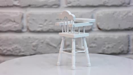 baby feeding chair painted white at the rotating table. carved wooden furniture item for kid's play. close up.