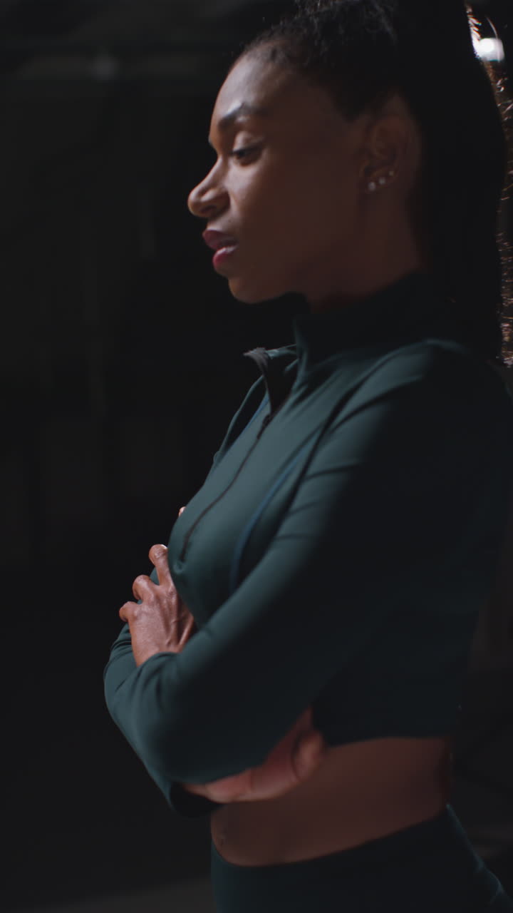 retrato de video vertical de una atleta femenina decidida en entrenamiento de trajes de entrenamiento en ropa de fitness filmado en el gimnasio con iluminación de bajo nivel