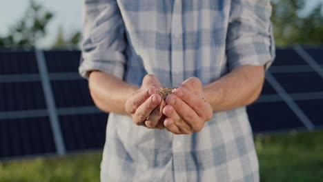 The-farmer-holds-a-handful-of-wheat-in-his-hands.-The-panels-of-the-solar-power-plant-are-visible-in-the-background.-Organic-farming-concept