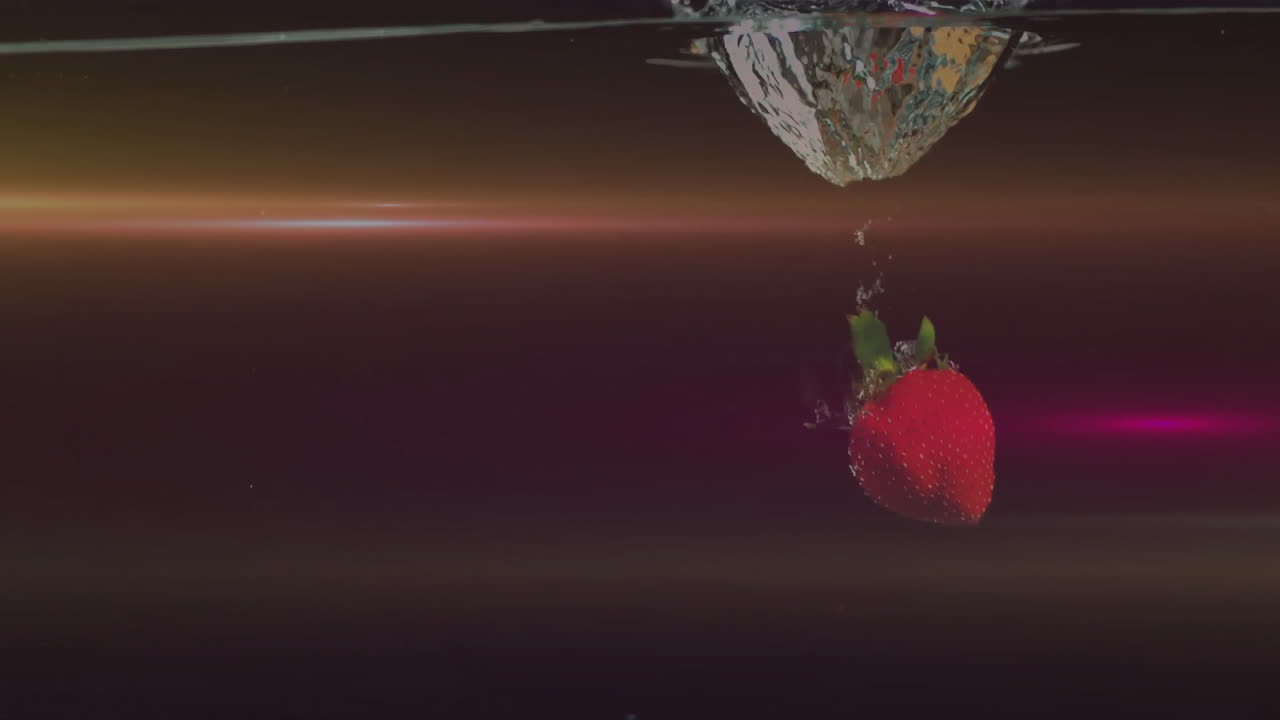 Animation of strawberry in water and light trails on black background
