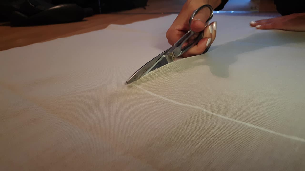 Primo piano delle mani di una sarta che tagliano il tessuto con le forbici in un atelier di cucito, statico con spazio per il testo