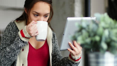 mujer tomando café mientras usa una tableta digital