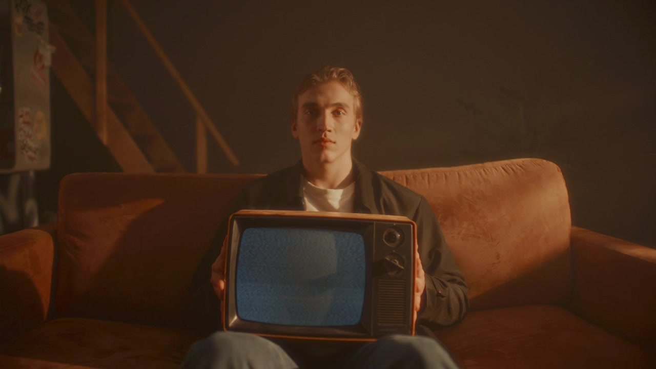 Ritratto di giovane seduto sul divano, con in mano una TV d'epoca con schermo a neve.