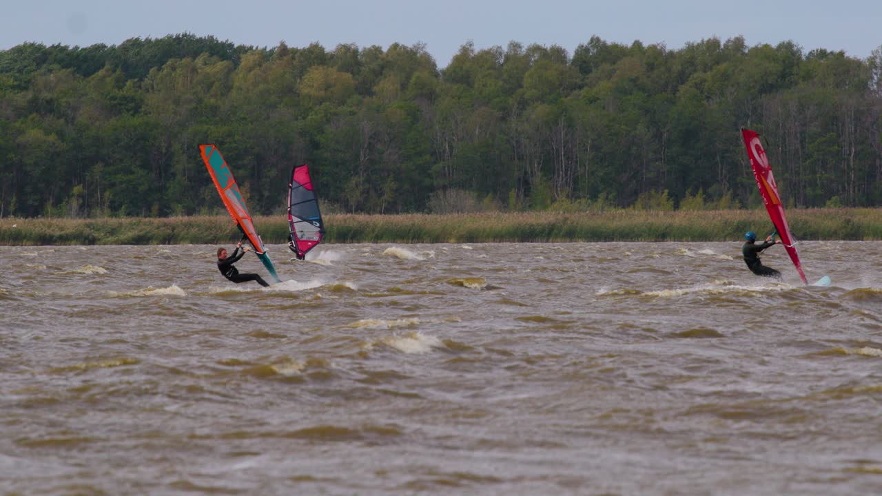 Three windsurfers surfing on lake in slow motion