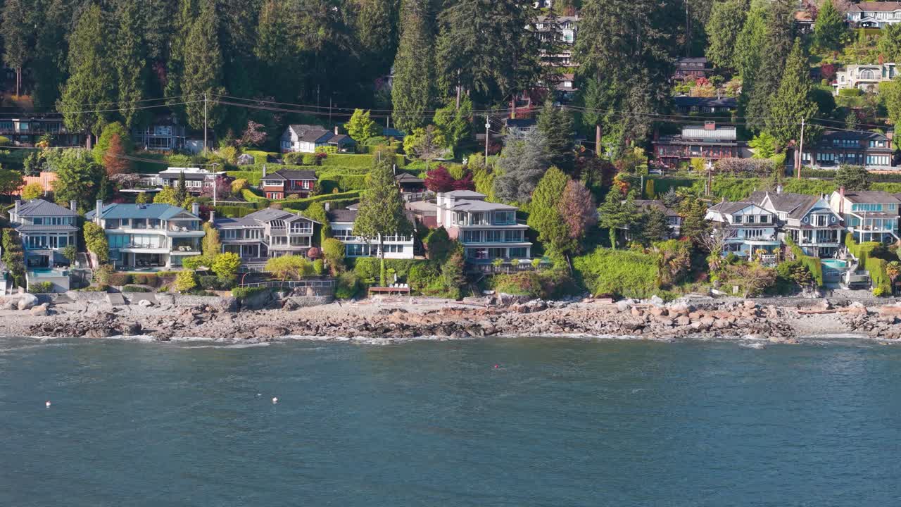 A scenic shot of multiple luxury homes surrounded by lush green trees along the coastline of west vancouver