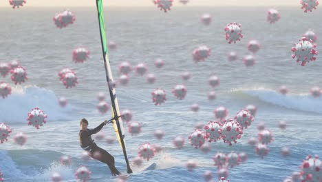 digital composite video of covid-19 cells moving against man windsurfing in the sea in background