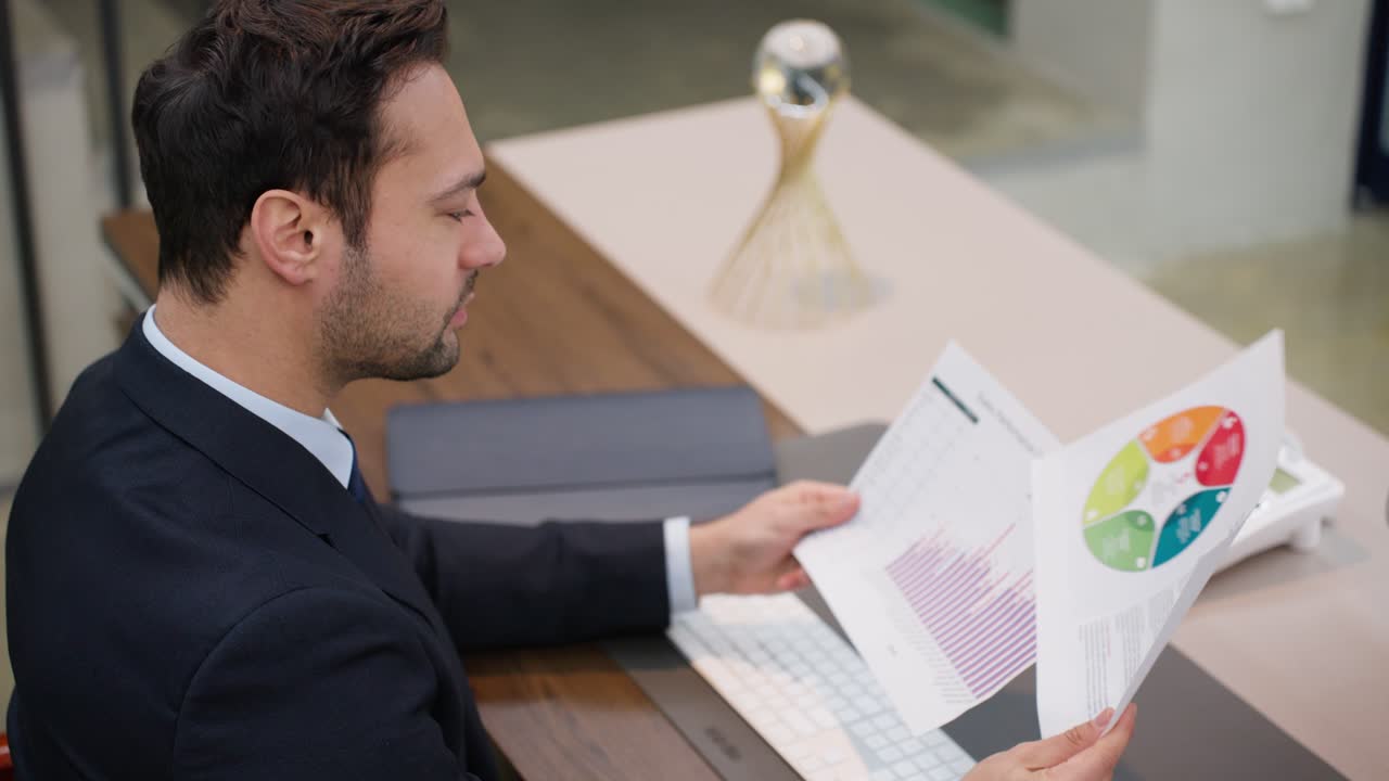 A professionally dressed man is seated at a desk, analyzing a printed bar graph chart at corporate office