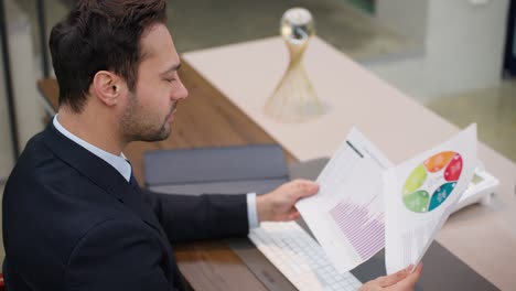 a professionally dressed man is seated at a desk, analyzing a printed bar graph chart at corporate office