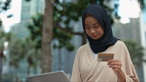 muslim woman shopping online with laptop and credit card outdoors