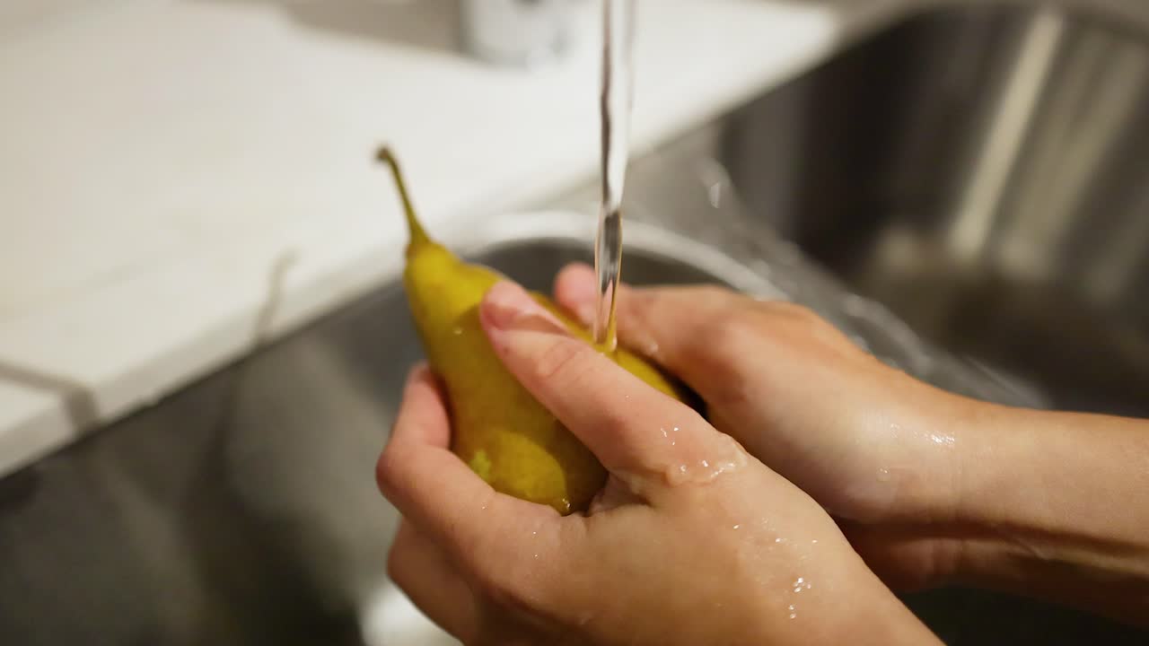 manos lavando una pera bajo agua corriente