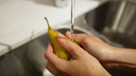 manos lavando una pera bajo agua corriente